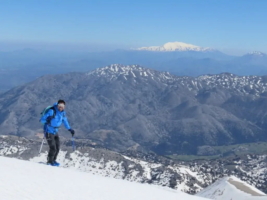 Ein Skifahrer in Winterbekleidung lächelt in die Kamera und genießt die verschneite Winterlandschaft mit majestätischen Bergen im Hintergrund.